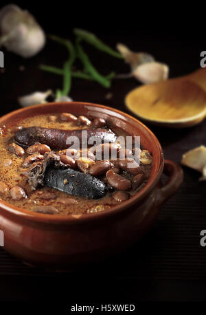 Fabada spagnolo con Black Pudding e salsiccia in un tegame di coccio su sfondo rustico Foto Stock