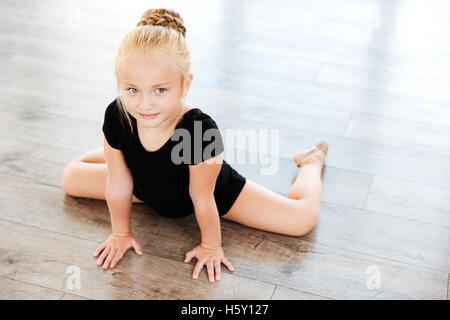 Carino bambina ballerina stretching sul pavimento in studio di danza Foto Stock