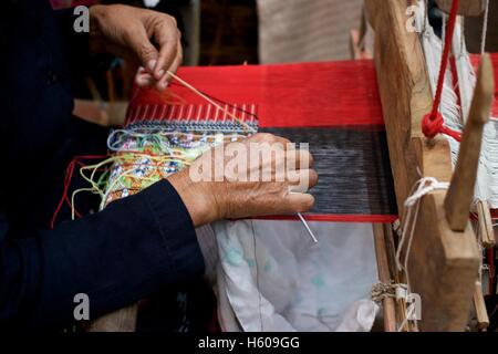 Donna vecchia tessitura di rosso e nero multi colore bandiera di cotone modello sul telaio nel nord della Thailandia Foto Stock