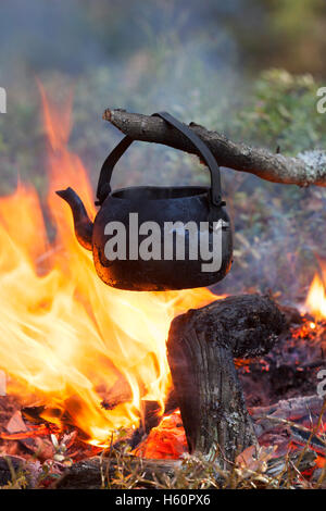 Stagno annerito bollitore dalla fuliggine acqua bollente su fiamme dal fuoco durante il trekking nella foresta Foto Stock