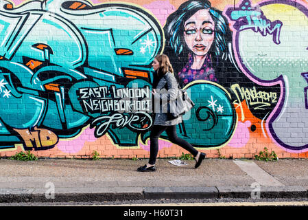 Giovane donna a piedi nella parte anteriore di un muro coperto di graffiti colorati in Shoreditch, East London, Regno Unito Foto Stock