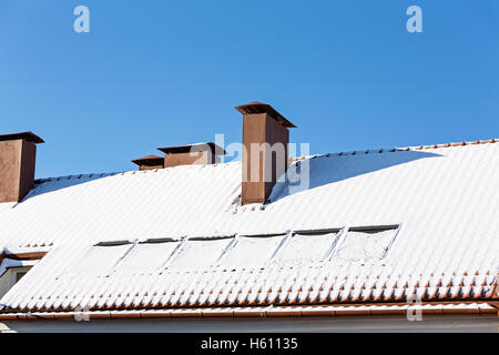 Camino marrone sul tetto di tegole rosse e coperto di neve Foto Stock