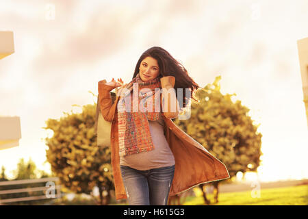 Donna incinta dopo lo shopping, felice speranzosi la ragazza con i sacchi di carta per andare a casa, dolce luce del tramonto, godendo grande vendita autunnale Foto Stock