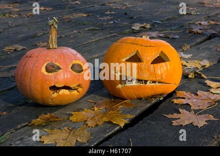 Due terribili brutto zucche su un pavimento in legno con foglie di acero nella notte. Foto Stock