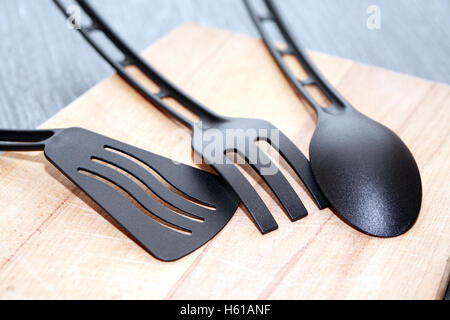 In plastica nera utensili da cucina sul tagliere di legno Foto Stock