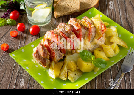 Carni cotte al forno con formaggio e pomodoro con patate al forno su di un tavolo di legno. Foto Stock