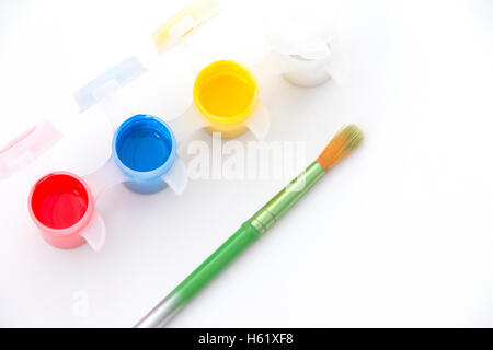 Paint Pots con vibrante rosso, giallo, blu e bianco paint, a fianco di un pennello di colore verde Foto Stock