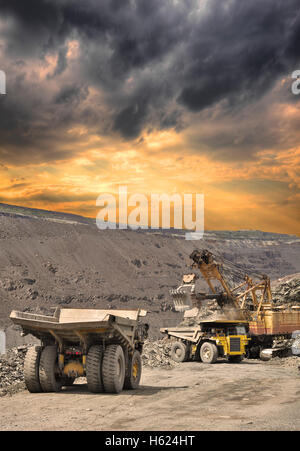 Heavy autocarri con cassone ribaltabile essendo caricati con minerali di ferro sul a cielo aperto sul tramonto tempestoso Foto Stock