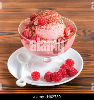Deliziosi dessert rosa ice cream scoop con lamponi freschi e cosparso di gocce di cioccolato in tazza su sfondo di legno, chiudi Foto Stock