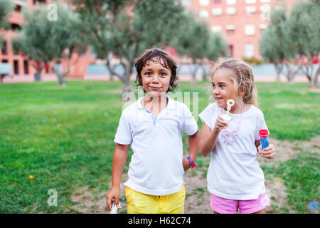 Bambina e ragazzo con anelli di bolle in un parco Foto Stock