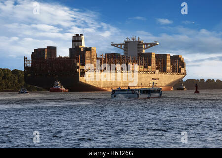 Contenitore nave che lascia il porto di Amburgo sotto la luce del sole di setting Foto Stock