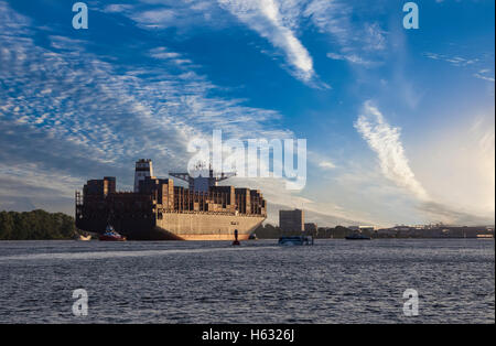 Contenitore nave che lascia il porto di Amburgo sotto la luce del sole di setting Foto Stock