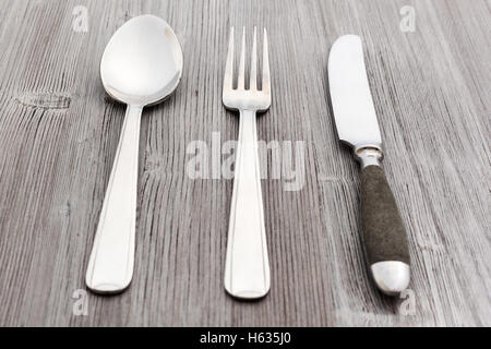 Concetto di cibo - set di posate da tavola coltello, forchetta, cucchiaio per minestra sul marrone chiaro pannello di legno Foto Stock