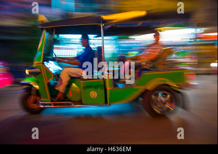 Un classico motorizzato di tuk-tuk taxi esegue lo zoom in una notte di sfocatura di luci al neon a Bangkok, in Thailandia Foto Stock