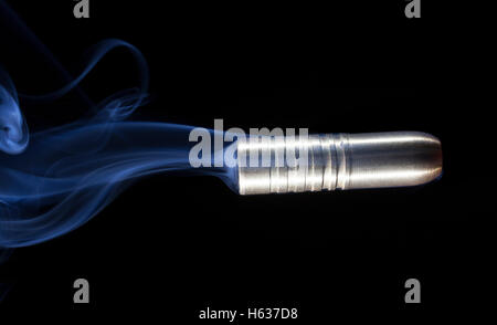 Colore rame bullet trainato da fumo blu su sfondo nero Foto Stock