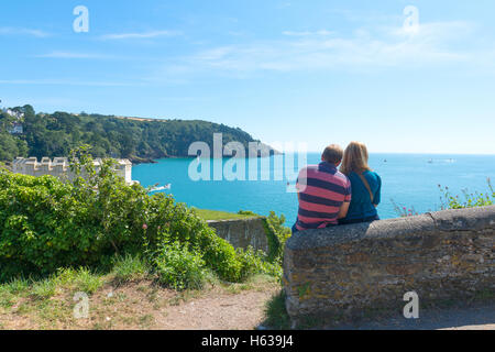 Coppia seduta su un muro di pietra che guarda verso il mare al castello di Dartmouth nel Devon in un pomeriggio estivo soleggiato Foto Stock