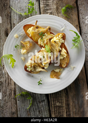 Giallo funghi Oyster saltate in burro e serviti con confuse uovo sulla pasta acida pane tostato con Wild Rocket Foto Stock