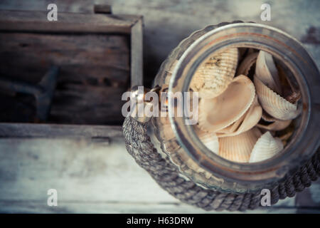 Vintage vecchio vaso di vetro con conchiglie di mare su sfocata sullo sfondo di legno con copia spazio. Vintage tropical still life Foto Stock