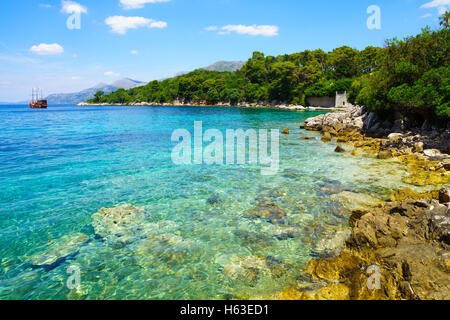 Una spiaggia rocciosa, barche e una nave, in Kolocep isola, una delle isole Elafiti, Croazia Foto Stock