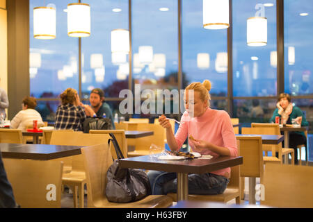 Giovane donna di mangiare pizza all'aeroporto ristorante mentre si è in attesa della partenza del volo. Foto Stock