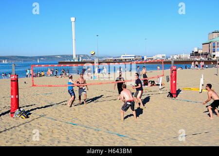 I villeggianti giocando a pallavolo sulla spiaggia con il padiglione e Jurassic Skyline tower per la parte posteriore di Weymouth, Regno Unito. Foto Stock