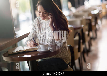 Bella donna che lavorano e studiano in cafe mentre si parla al telefono Foto Stock
