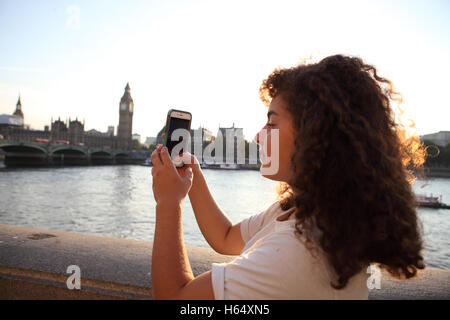 Un sedicenne adolescente israeliano, un turista, usa il suo smartphone al tramonto per fotografare alcune di Londra Attrazioni turistiche Foto Stock