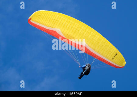 Un appassionato di parapendio vela Tettuccio posizionato al di sotto di un rosso e giallo di parapendio 0n un estati soleggiate giornata contro un profondo cielo blu Foto Stock
