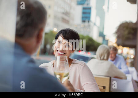 Coppia sorridente tostare calici da bianco a livello urbano sidewalk cafe Foto Stock