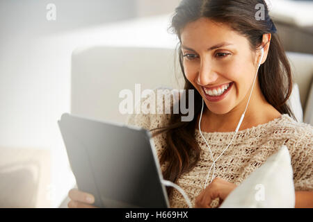 Donna sorridente con tavoletta digitale con le cuffie sul divano Foto Stock