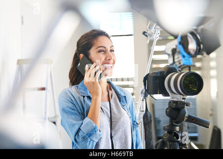 Donna sorridente fotografo parlando al cellulare dietro la telecamera in studio Foto Stock