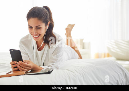 Donna sorridente ascolto di musica con cuffie e lettore mp3 sul letto Foto Stock