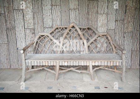 Panca in legno realizzato da rami in un gazebo con uno sfondo di legno in un giardino a Dunham Massey, Cheshire, Inghilterra, Regno Unito Foto Stock