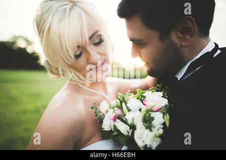 Lo Sposo è holding e baciando la sua sposa sullo sfondo tramonto Foto Stock