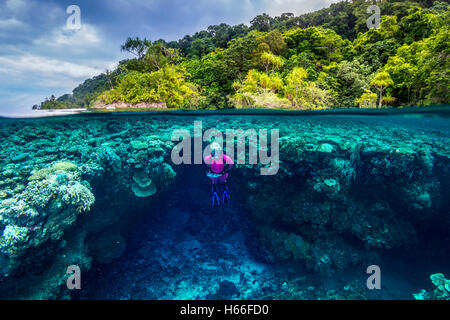 Immagine sdoppiata colpo di donna bionda scuba diver esplorare la barriera corallina con isola tropicale in background Foto Stock