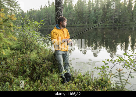 L uomo è la pesca sulle rive del bellissimo lago di foresta Foto Stock