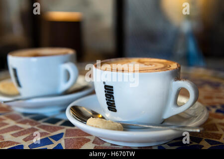 Due cappuccini sul tavolo a mosaico in origine le tazze di caffè con biscotti e cucchiai Foto Stock