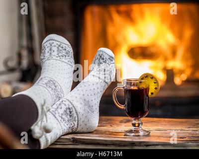 Riscaldamento e rilassarsi vicino al camino. Donna piedi vicino alla tazza di vino caldo nella parte anteriore del fuoco. Foto Stock