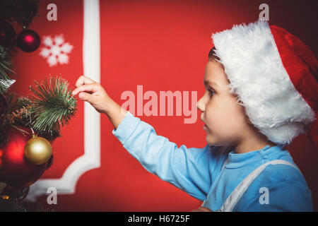 Bel ritratto di Little Boy in Santa hat decorare l'albero di Natale Capodanno Camera. L idea per cartoline. Soft focus. S Foto Stock