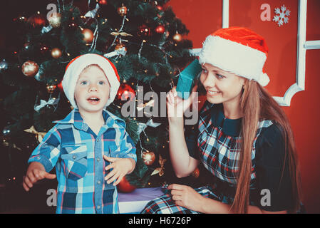 Bel ritratto di felice madre e figlio sullo sfondo dell albero di natale nel nuovo anno camera con doni. L'idea per il pos Foto Stock