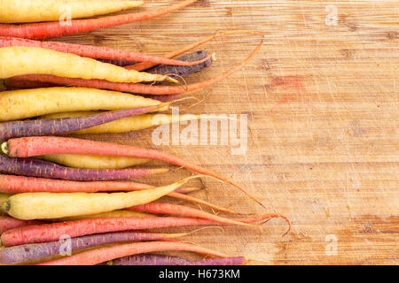 Confine della varietà colorate di intere materie le carote fresche disposto a lato di un bordo di taglio con spazio copia pronta per essere prep Foto Stock