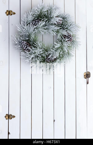 Nevoso inverno ghirlanda di Natale con satinato verde fresche fronde di pini e coni appeso sulla porta del granaio di bianco legno tinto con Foto Stock