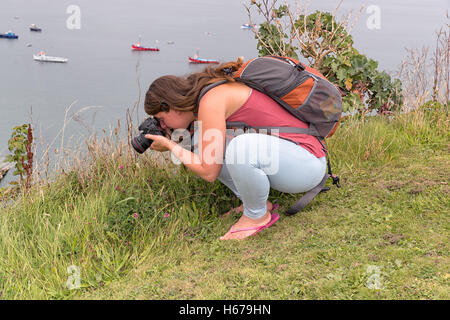 Fotografo femminile accovacciato verso il basso facendo qualche fotografia macro esterno con il mare sullo sfondo. Foto Stock