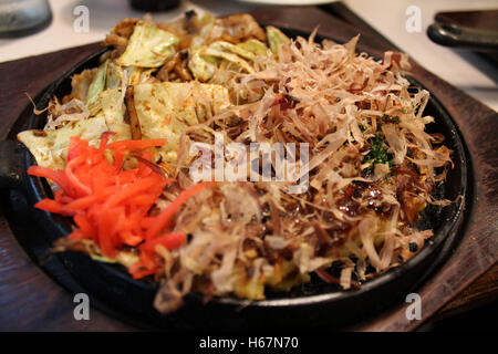 Okonomiyaki, Giapponese Pizza guarnita con scaglie di Bonito e affettato decapati lo zenzero in un ferro da stiro caldo padella a Kyoto, Giappone Foto Stock