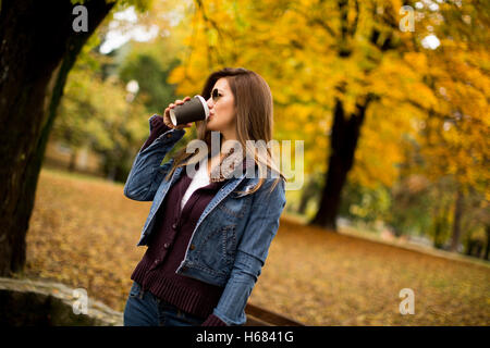 Giovane donna con il caffè per andare in autunno park Foto Stock