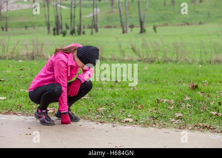 Giovane atleta femminile esaurito dopo l'esecuzione in una fredda giornata invernale in pista di un parco urbano. Foto Stock