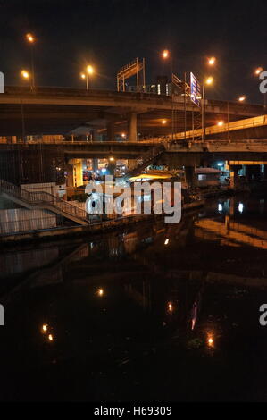 Una delle baraccopoli sotto diverse autostrade in sul dado district, Bangkok, Thailandia, lungo il fiume di notte. Foto Stock