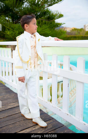 Ragazzo con il bianco sailor suit appoggiata su una bianca staccionata in legno su un ponte nella sua Prima Comunione Foto Stock