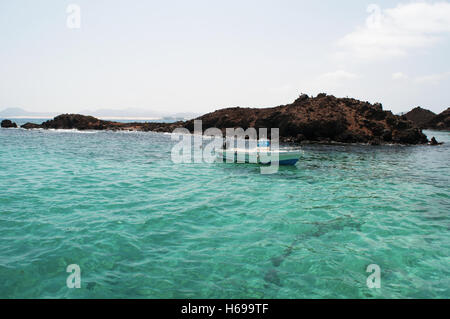 Isole Canarie, Nord Africa, Spagna: una barca, le acque cristalline e nero ocks sulla piccola isola di Lobos, 2 chilometri a nord di Fuerteventura Foto Stock