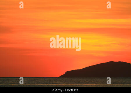 Tramonto sull'oceano con una silhouette di un promontorio nella distanza di rosso e un cielo arancione Foto Stock